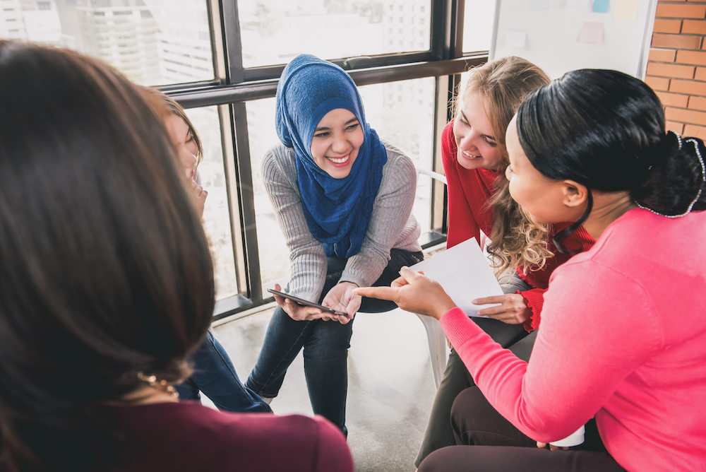 Diverse women sitting in circle enjoying sharing stories in group meeting